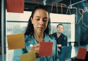 People looking at post-it notes on a wall in office