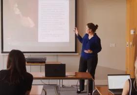 A woman stands and presents at the front of a classroom.