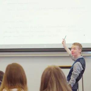 Academic stood at front of classroom pointing at projection of teaching materials