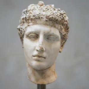 A clay bust of Augustus with closed eyes, displayed against a plain grey wall