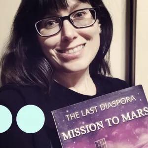 Woman with brown hair and glasses smiling and holding a book