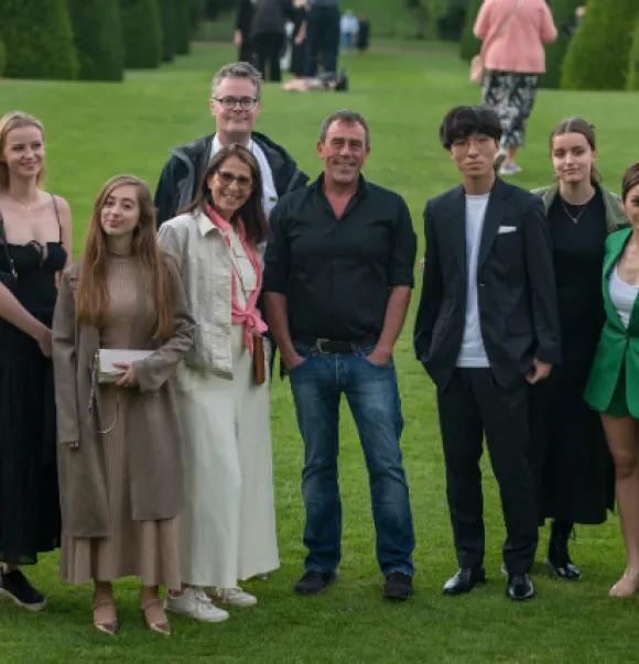 A group of 11 students standing and smiling on a green lawn.