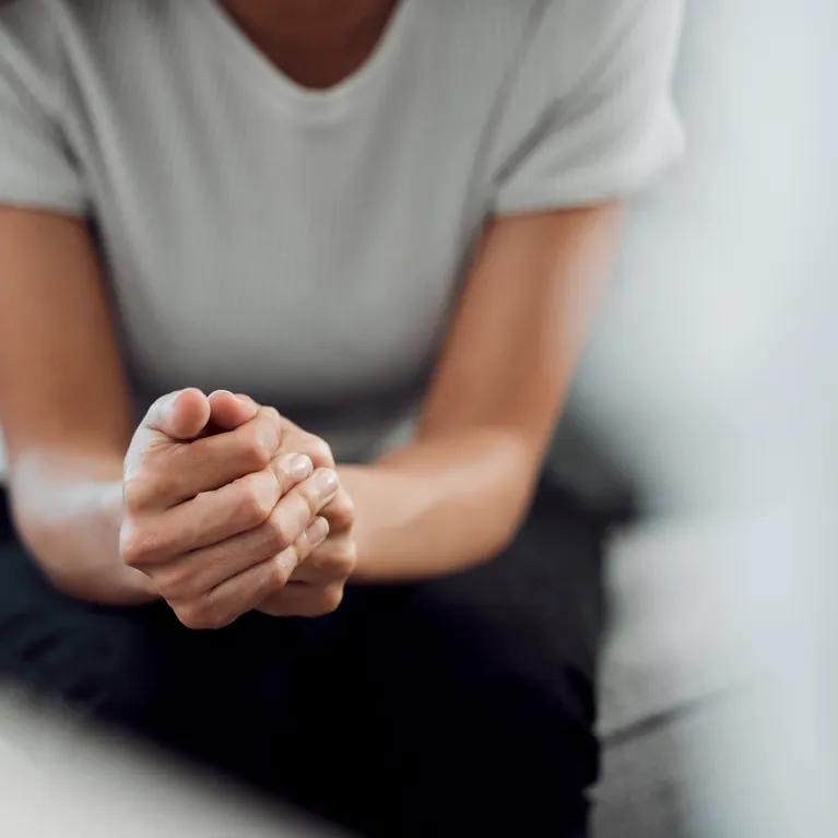 A person with clasped hands leaning forward on a couch