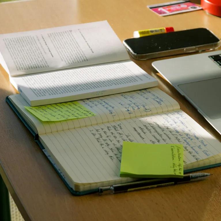 A student's desk with laptop, note book, text book and phone