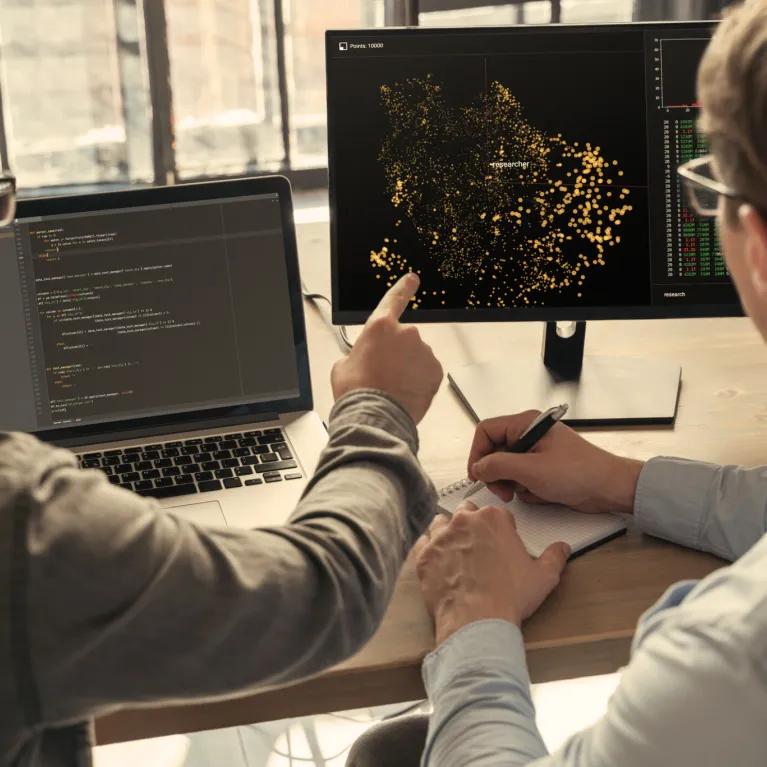 Two people discussing data at 2 computers 