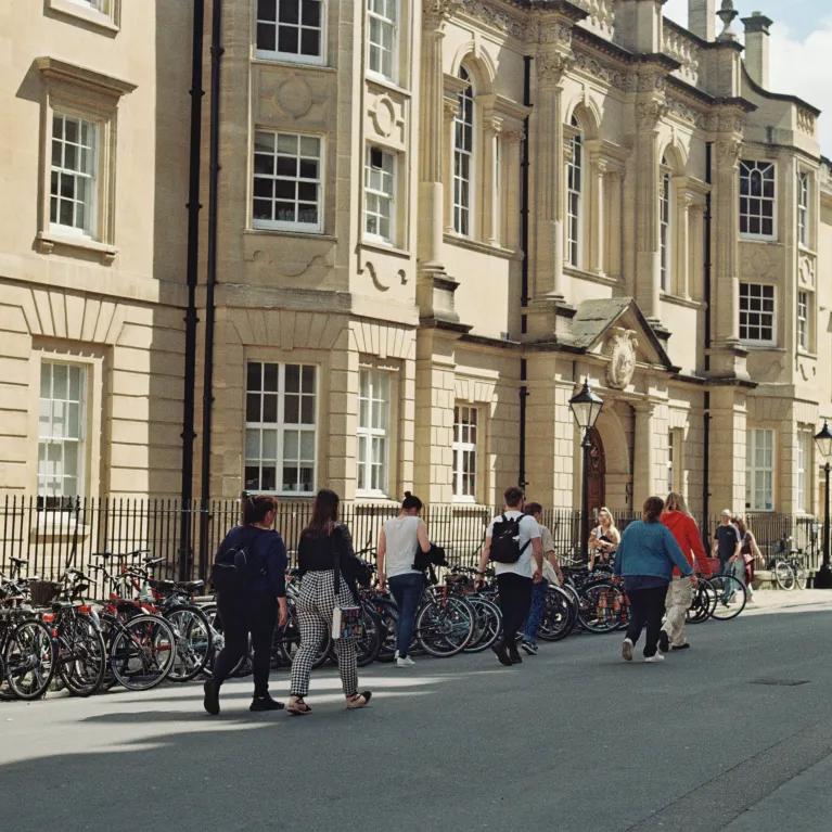 Pedestrians walk past the facade of a Cambridge University building.