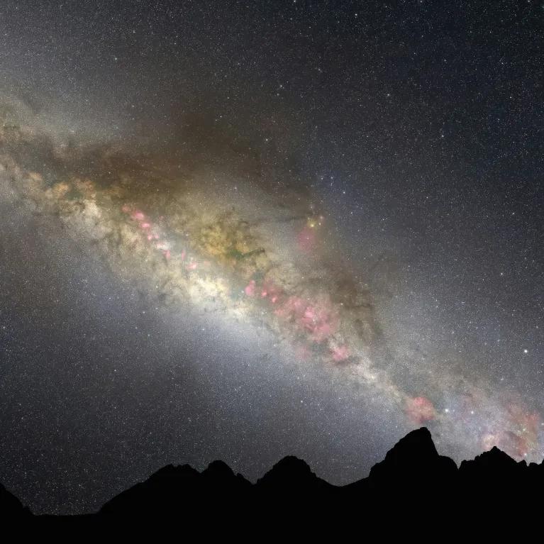 A silhouette of mountains beneath a starry night sky, with subtle colours of the galaxy visible among the stars.