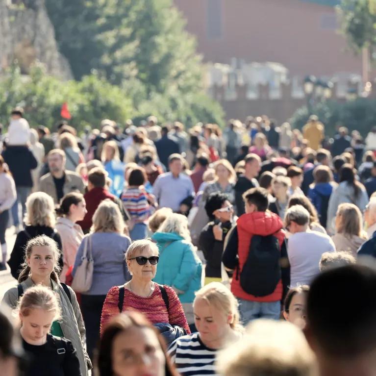 Photograph of everyday people walking about on a wide path with buildings in background