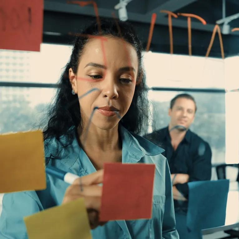 People looking at post-it notes on a wall in office