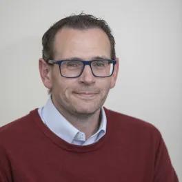 Headshot of smiling man wearing a white shirt, maroon jumper and glasses.